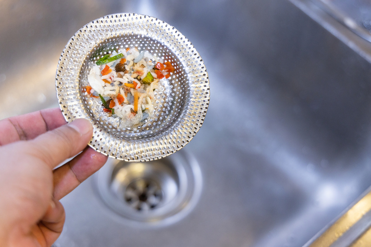 Hand holding kitchen sink waste filter with trapped food waste.